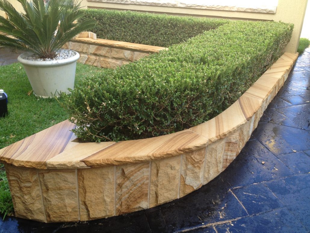 Curved sandstone wall with capping around a hedge